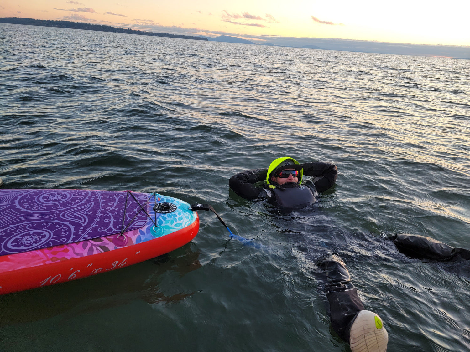man swimming beside paddle board